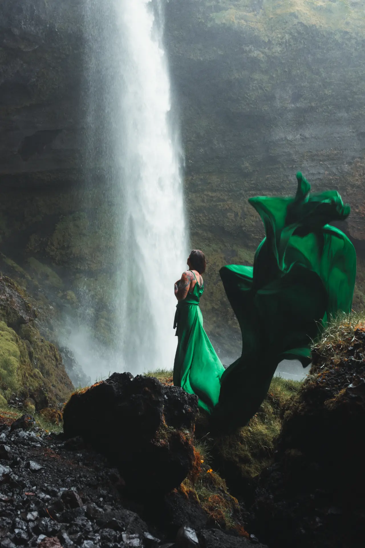 Woman in a flowing emerald gown before a tall waterfall