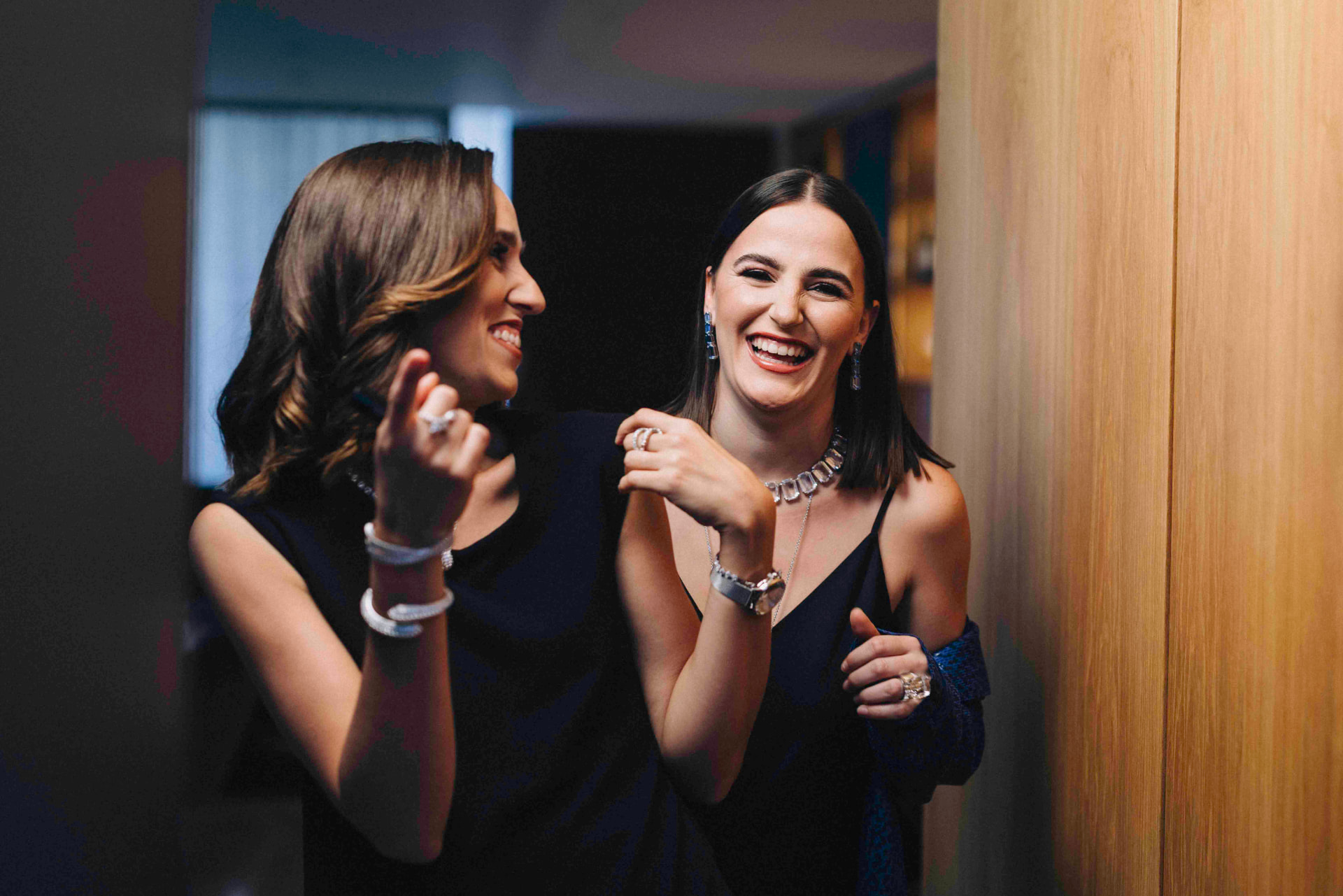 Two women in navy evening dresses laughing while wearing high jewellery