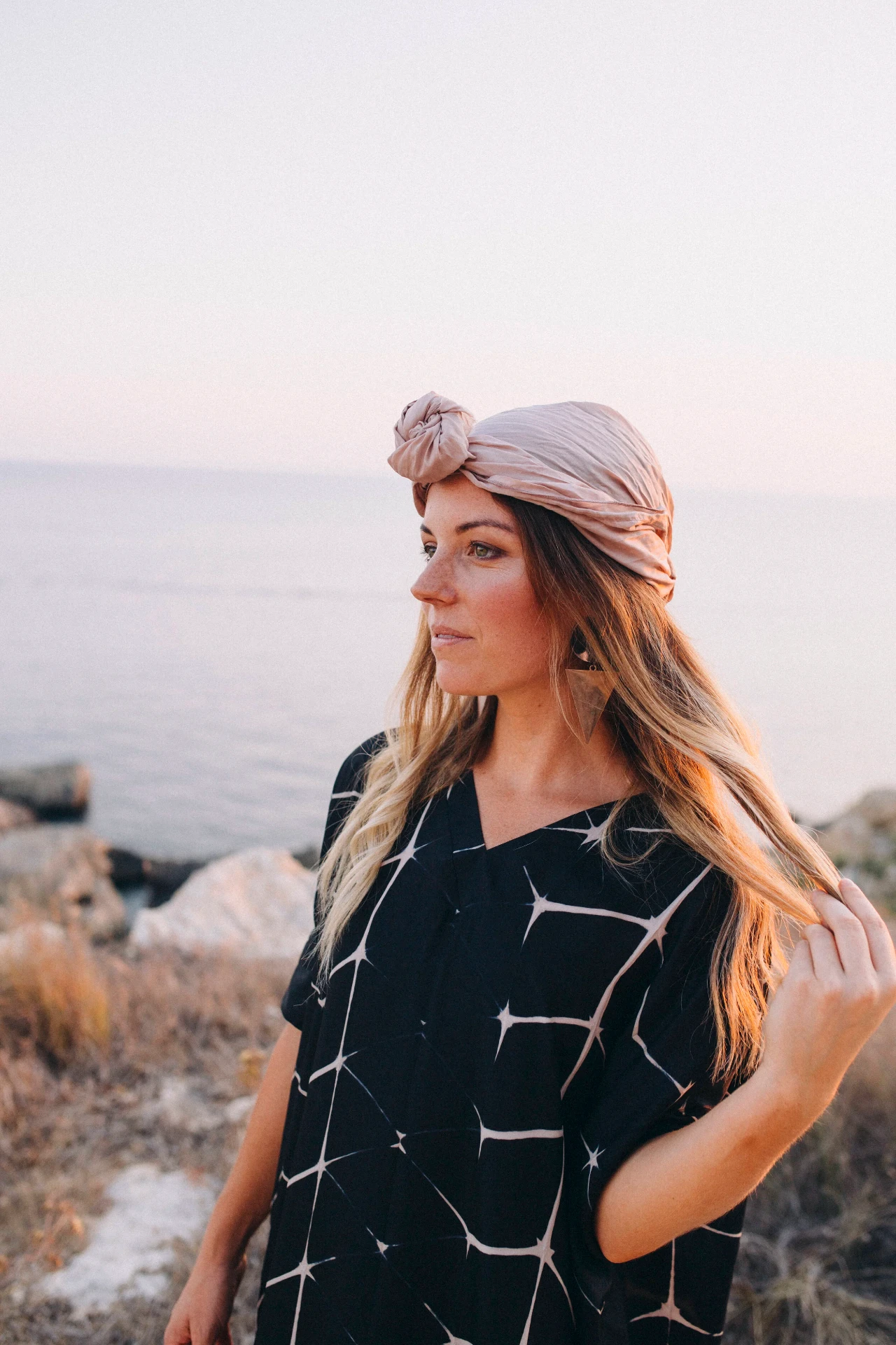 Model in a blush turban and black shibori kaftan at sunset by the sea
