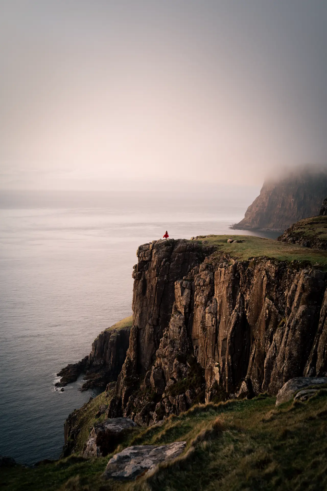 Figure in red on a sea cliff at Neist Point in soft mist